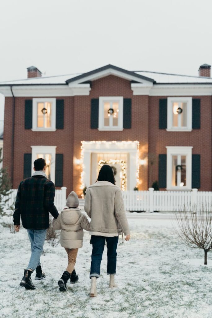 A family walks towards a beautifully decorated house on a snowy winter day, creating a warm holiday atmosphere.